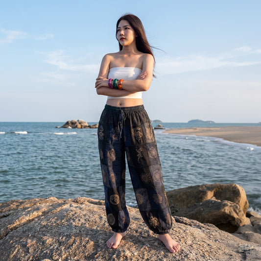 Female model enjoying the breeze on beach rocks in black stonewashed organic cotton tribal harem pants.