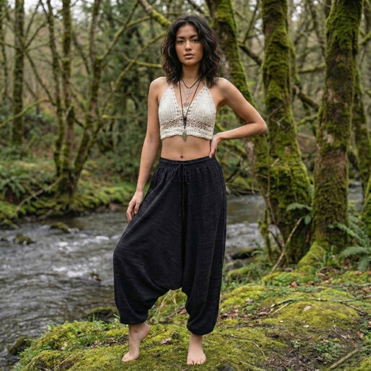Woman standing in a forest with a stream in the background wearing black pinstripe thai harem pants and white top