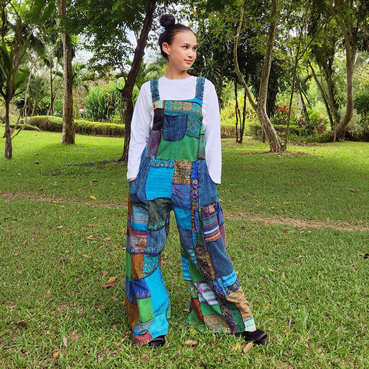 Female model wearing blue patchwork jumpsuit overall in a park, front view.