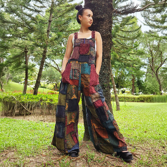Female model wearing brown patchwork overall jumpsuit in a park, front view.