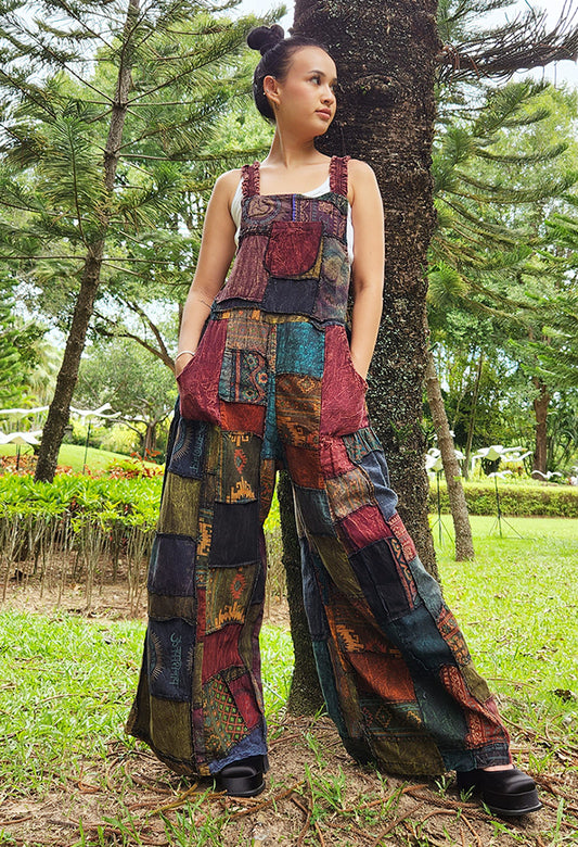Female model wearing brown patchwork overall jumpsuit in a park, front view.