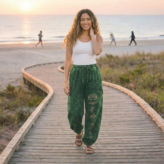 Female model wearing green boho lotus festival harem pants on a wooden path at the beach, front view.