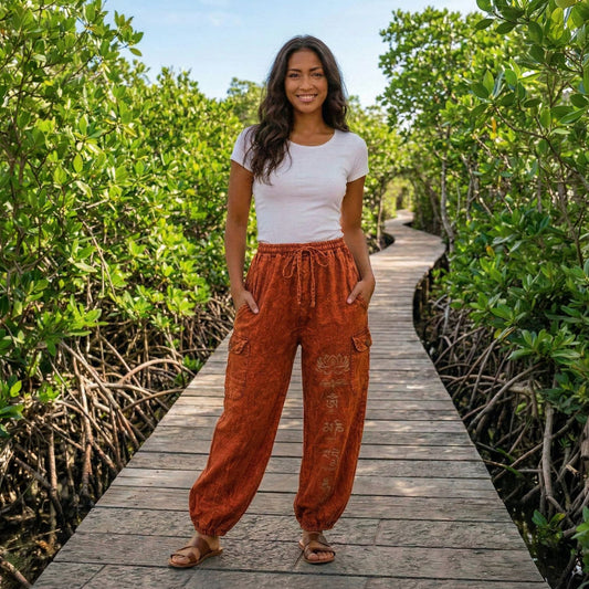 Female model wearing orange boho lotus festival harem pants on a boardwalk through mangroves, front view.