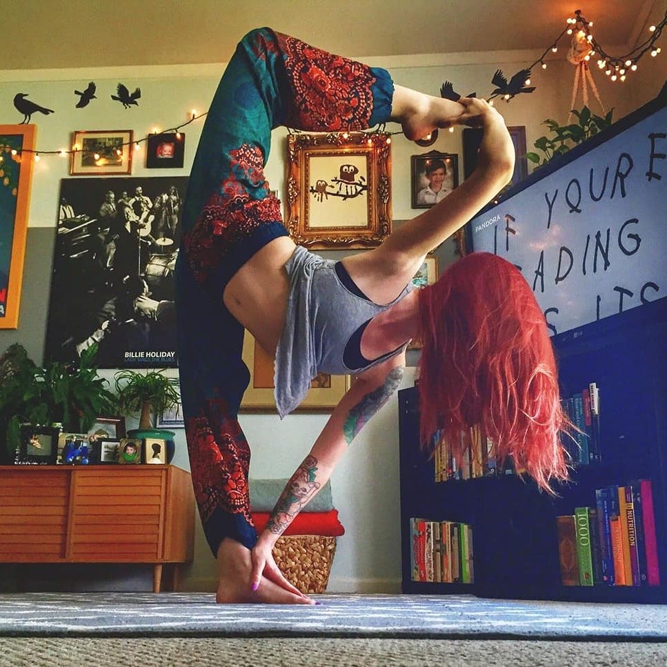 Woman with red hair wearing turquoise Thai harem yoga pants with mandala print and grey top practicing yoga indoors