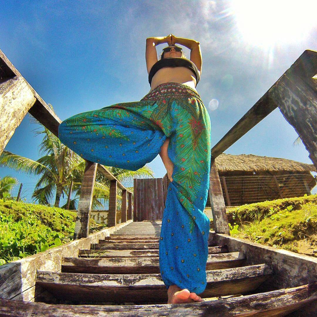 Woman in a blue Thai harem yoga pants standing on a wooden staircase with a tropical setting.