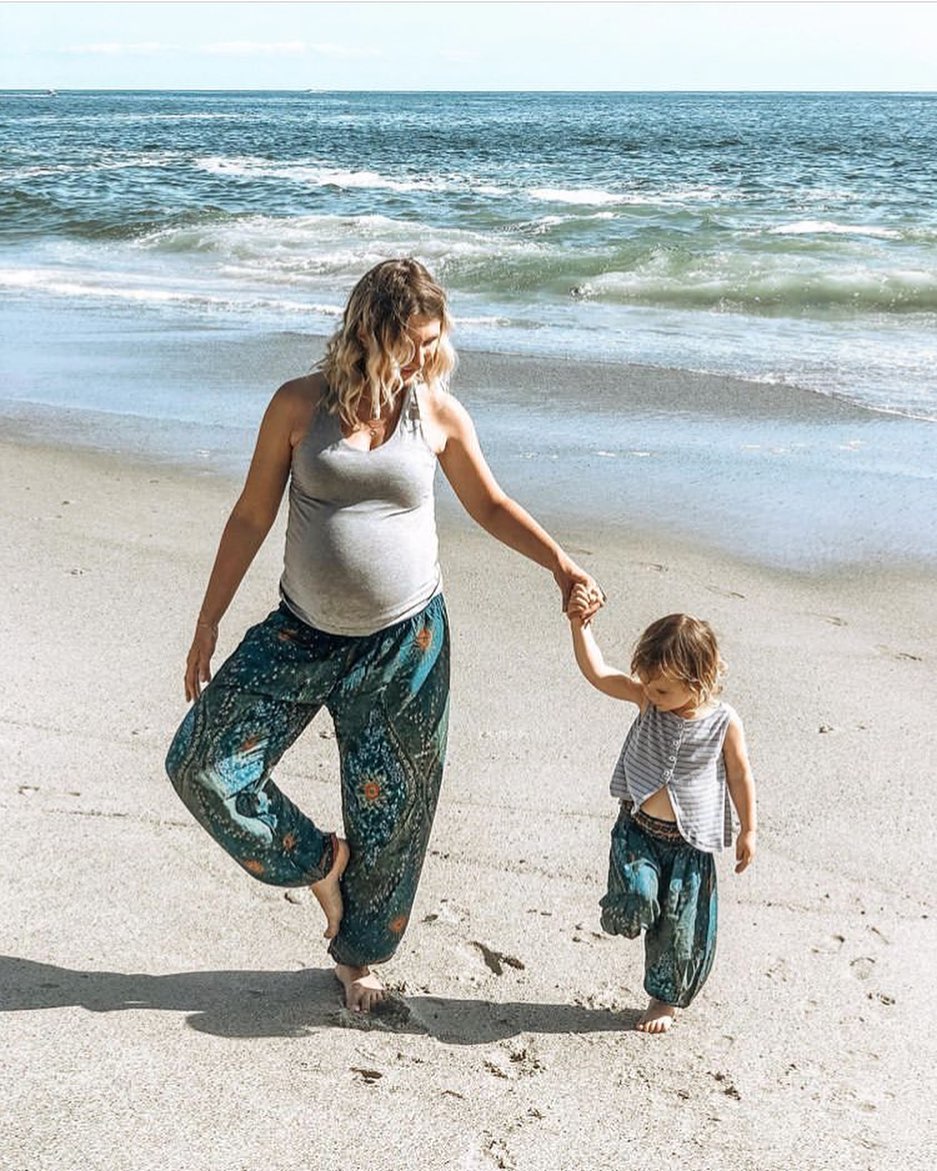 Woman and child both wearing turquoise Thai harem yoga pants with peacock print and rey top holding hands on a beach