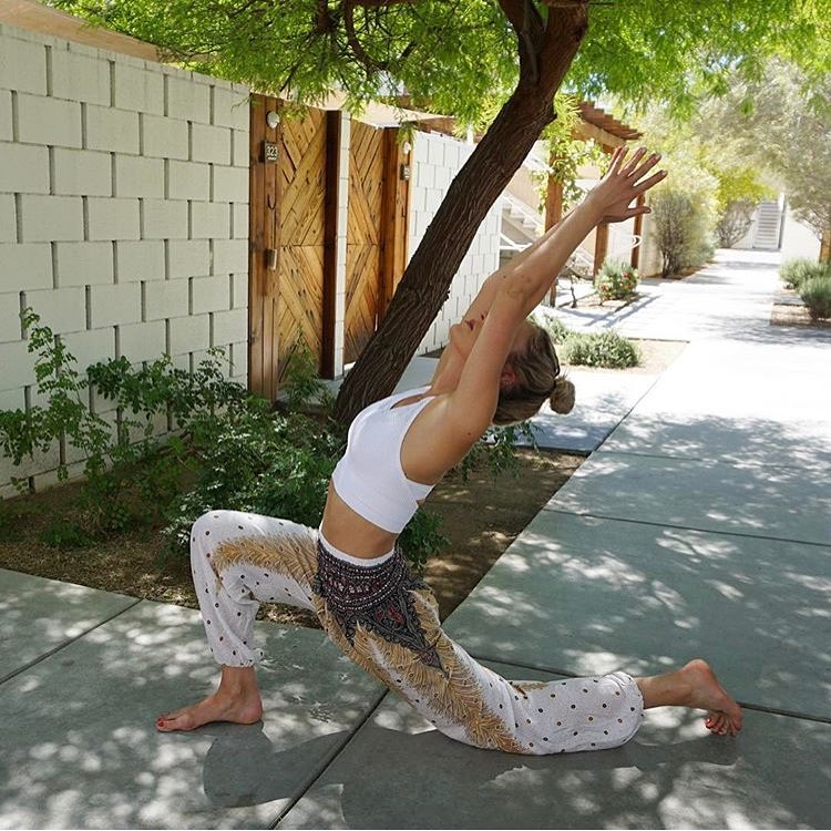 Person in white Thai harem yoga pants with peacock print and white top practicing yoga outdoors on a sunny day