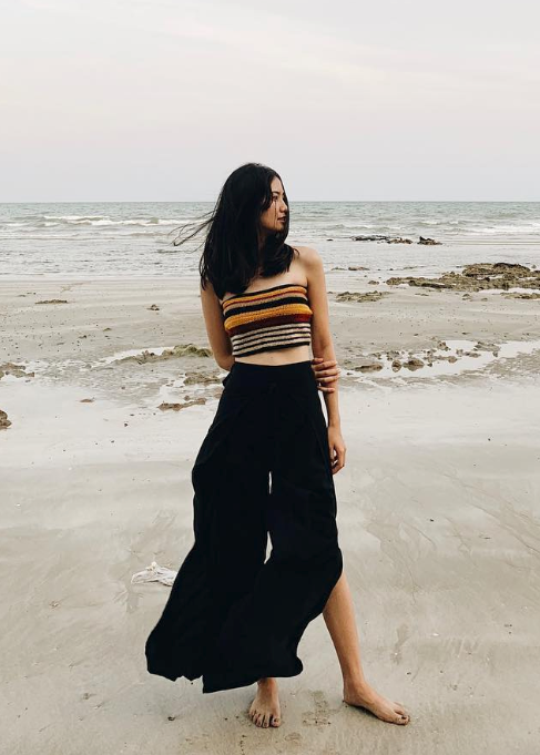 Woman in black thai wrap pants skirt and brown top standing on a thai beach