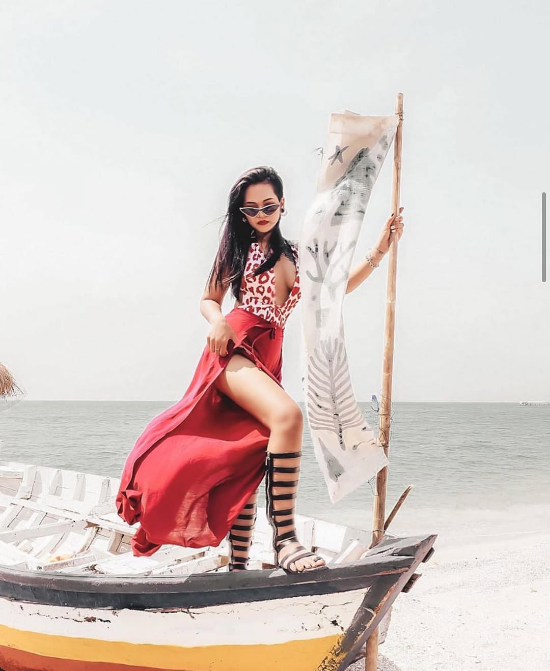 Woman in a red thai wrap pants skirt and leopard print top standing on a boat with a white background