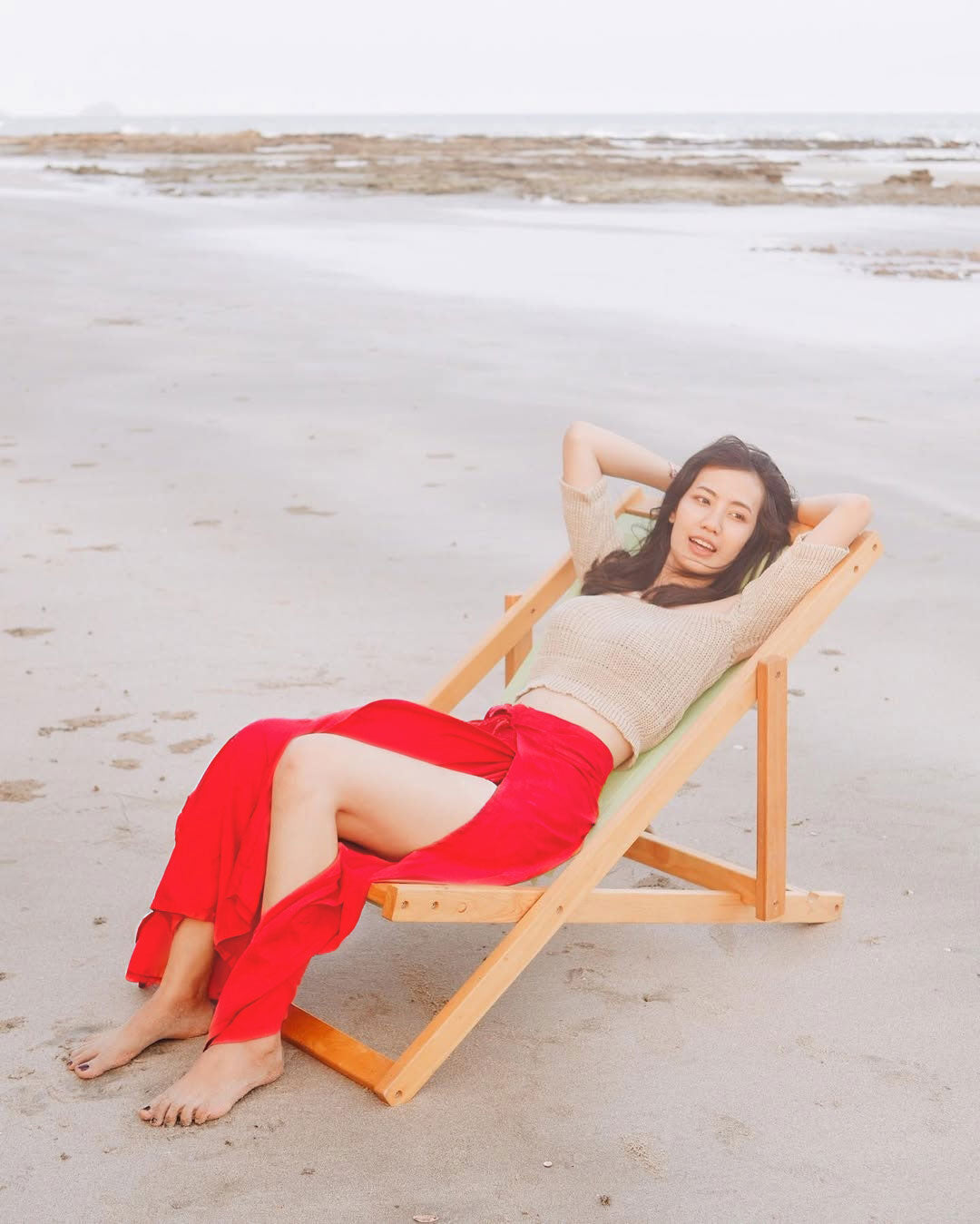 Woman in red Thai wrap pants skirt and beige top relaxing on a beach chair at the beach