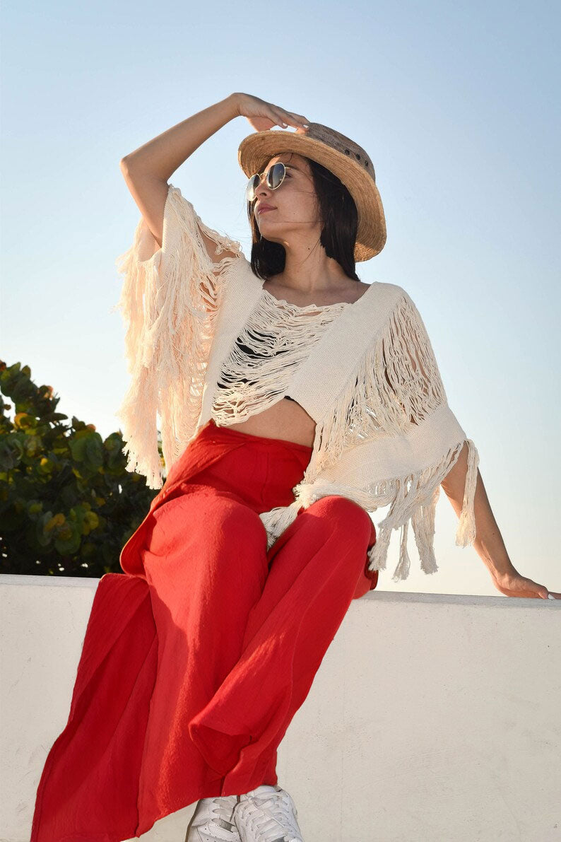 Woman in a white fringe top and red thai wrap pants skirt sitting on a ledge with a blue sky background