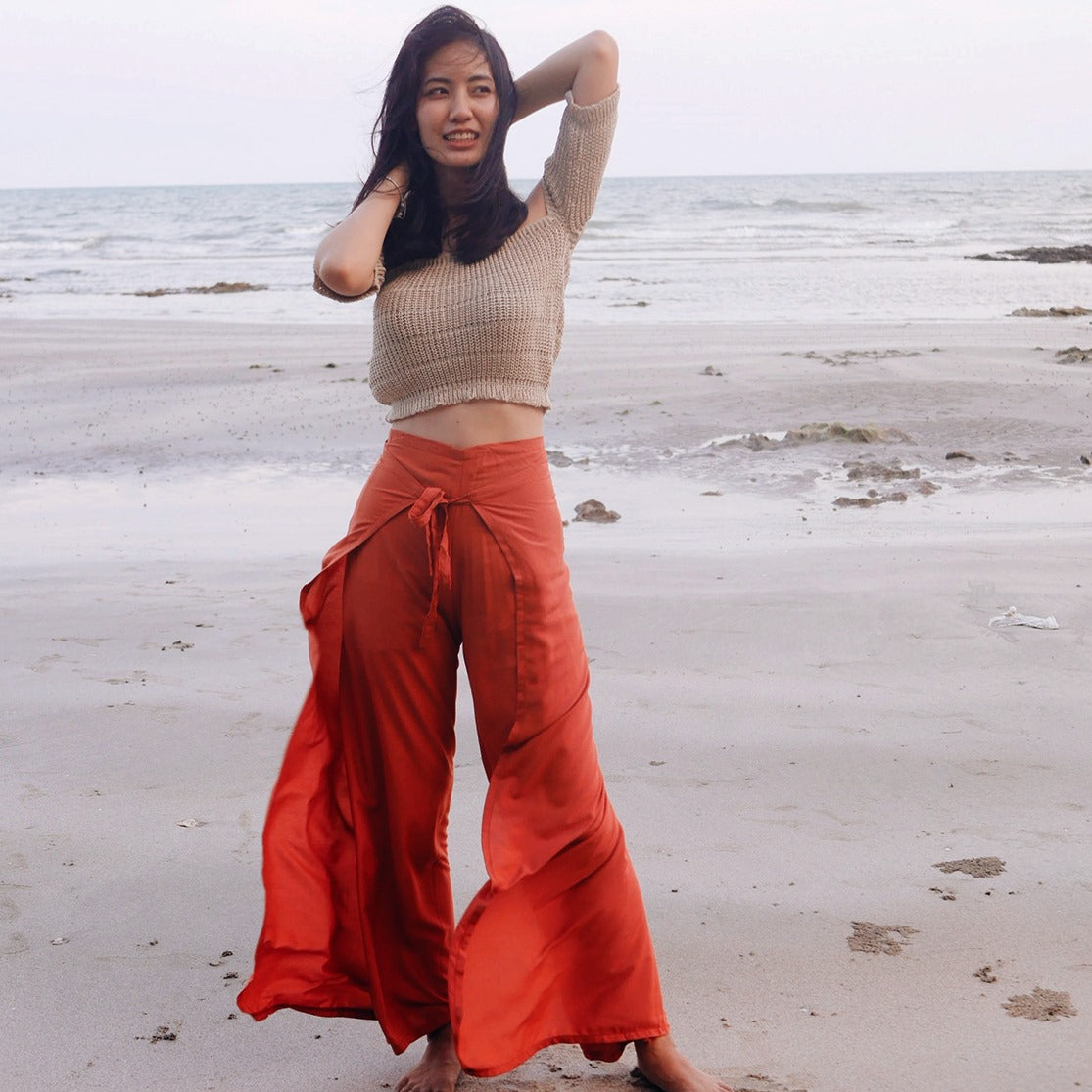 Woman in red thai wrap pants skirt and beige top standing on a thai beach