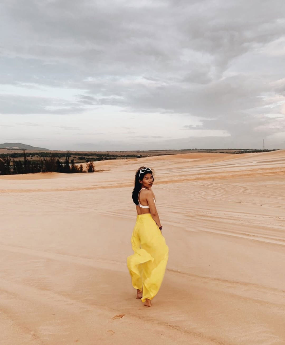 Woman in a yellow thai wrap pants skirt standing in a desert landscape with a cloudy sky.