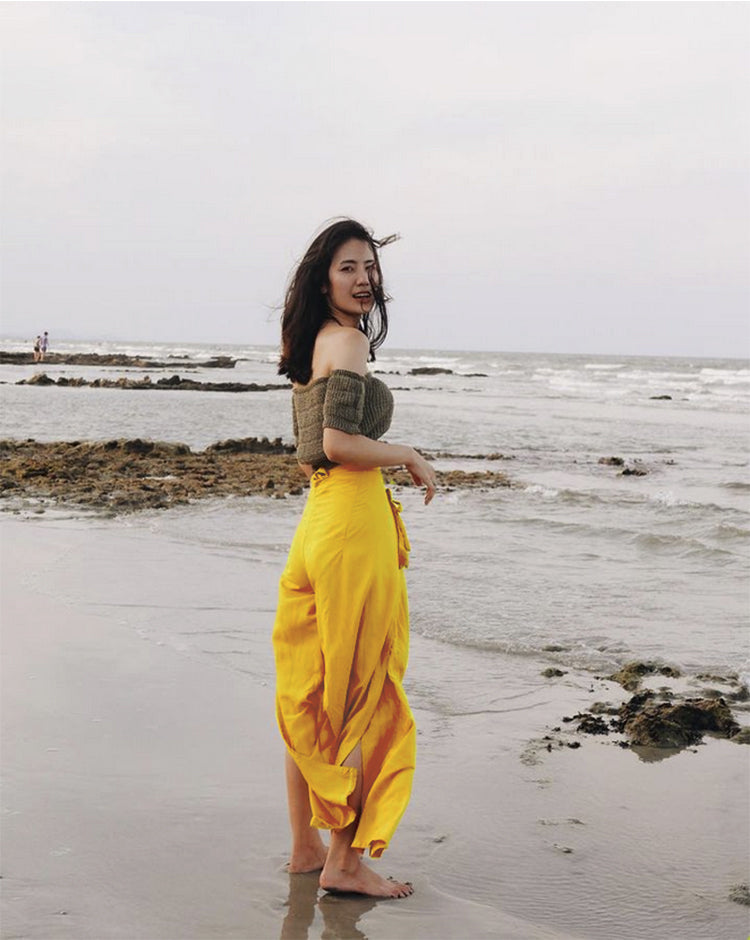 Woman in yellow thai wrap pants skirt and green top standing on a thai beach