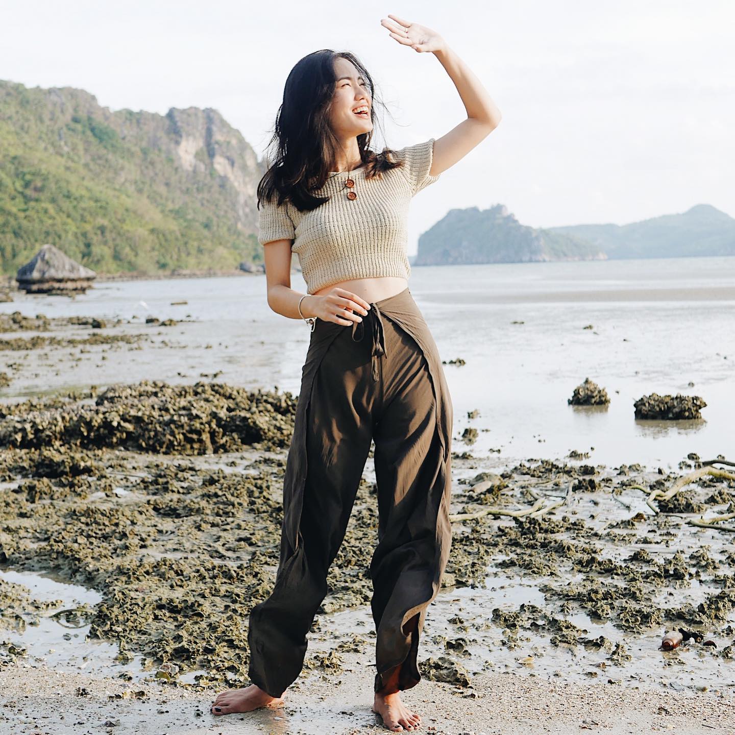 Woman in brown thai wrap pants skirt and beige top standing on a thai beach