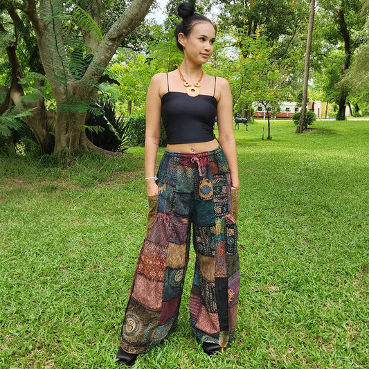 Female model wearing black patchwork wide-leg hippie palazzo boho pants in a park, front view.