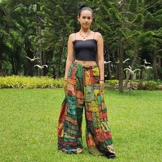 Female model wearing brown patchwork wide-leg boho palazzo pants standing in a sunny park, front view.