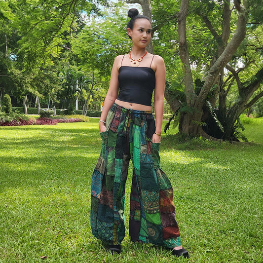 Woman wearing green patchwork wide-leg boho palazzo pants in a lush green park setting, front view.