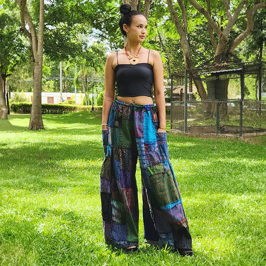 Female model posing in purple patchwork wide-leg palazzo boho pants in a bright park environment.