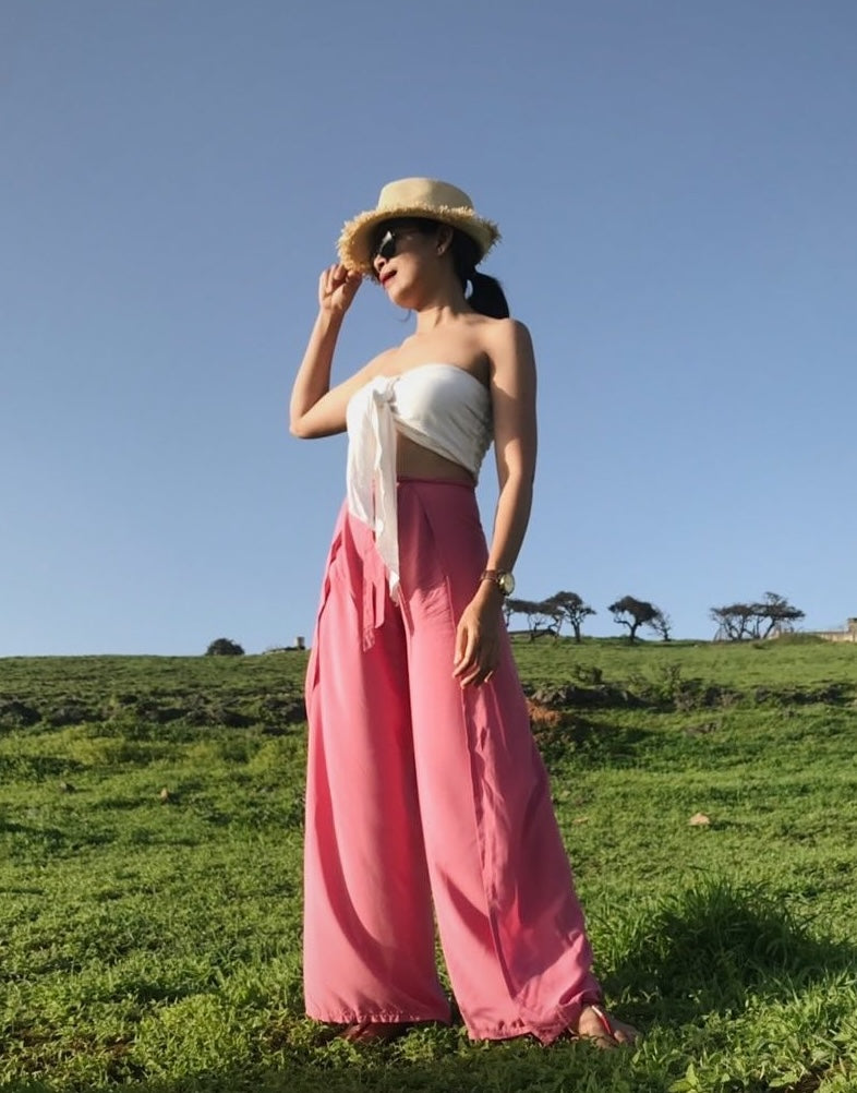 Woman wearing pink Thai wrap pants skirt with white top standing on grass
