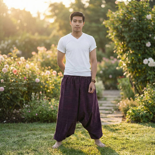 Man wearing a white t-shirt and purple Thai harem yoga pants standing in a garden with flowers and greenery.