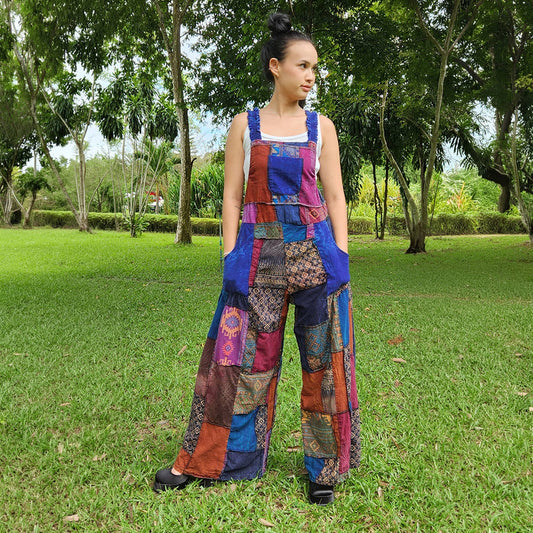 Female model wearing purple patchwork overall jumpsuit in a park, front view.