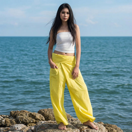 Female model standing confidently on rocks by the ocean, wearing versatile Golden Sunshine women's Thai fisherman pants.