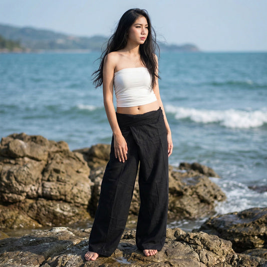 Female model standing confidently on rocks by the ocean, wearing versatile Midnight Black women's Thai fisherman pants.