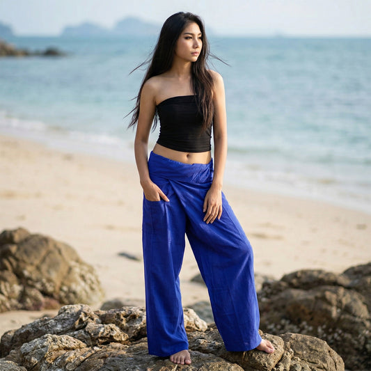 Female model standing confidently on rocks by the ocean, wearing versatile Oceanic Navy women's Thai fisherman pants.
