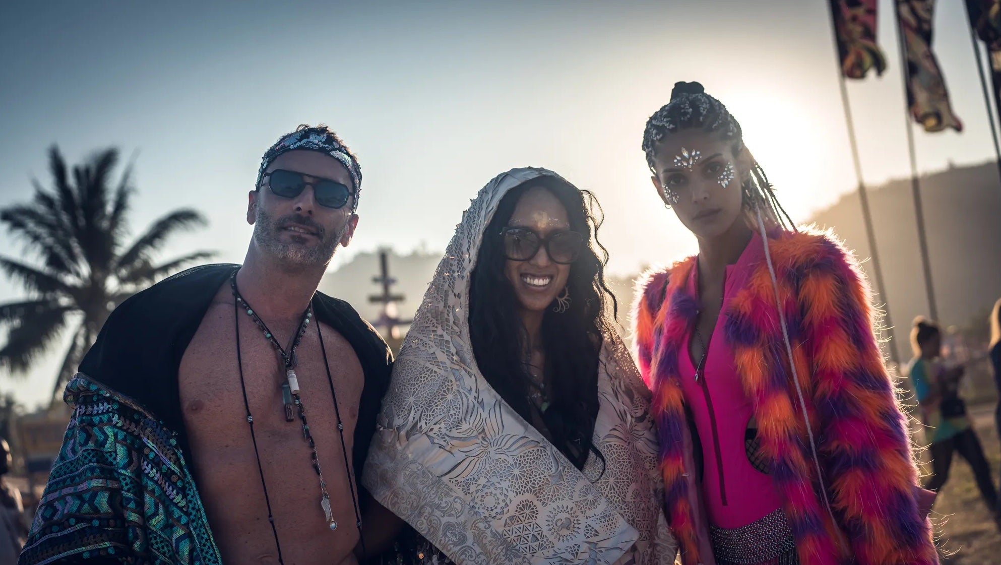 Three people posing together at Tomorrowland Thailand on a beach with palm trees in the background