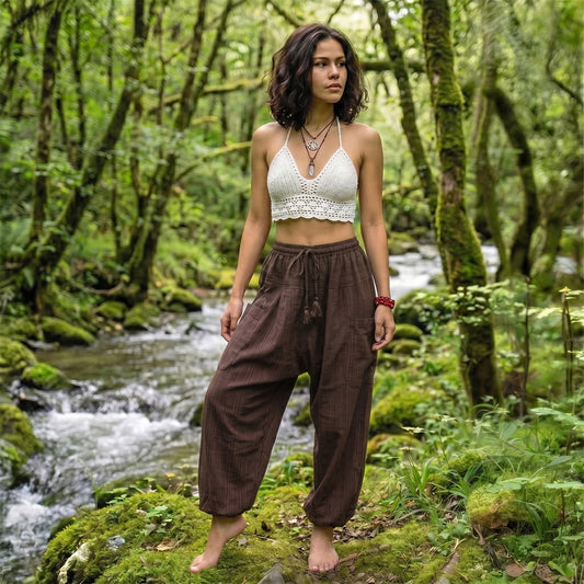 Model relaxing in Earthy Brown pinstripe pants near a flowing water source in the woods.