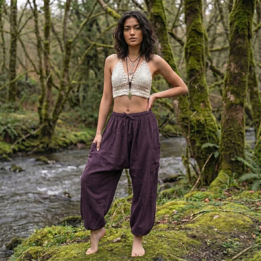 Female model wearing Purple Orchid pinstripe pants in a serene forest setting by a flowing stream.