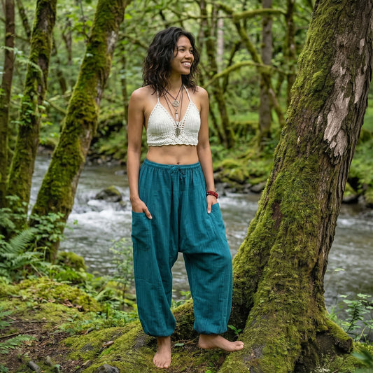 Female model wearing Turquoise Bay pinstripe harem pants in a forest setting by a flowing stream, showcasing the airy and flowy nature of the cotton.