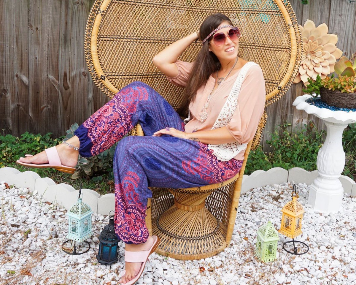 Woman in purple Thai harem yoga pants with mandala print and beige top sitting outside on a chair in a casual outdoor garden setting