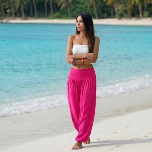 Female model in pink paradise Thai harem pants walking on a Thai beach, showcasing the airy, flowing color.