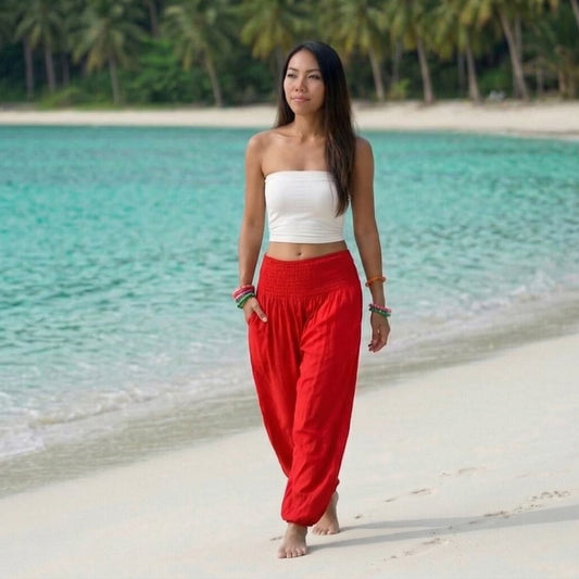 Female model in sunset red Thai harem pants walking on a Thai beach, showing the flexible fit and ultimate comfort of the ethnic clothing.