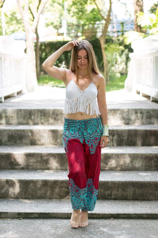 Woman wearing a white top and a red Thai harem yoga pants with teal lace details walking down steps