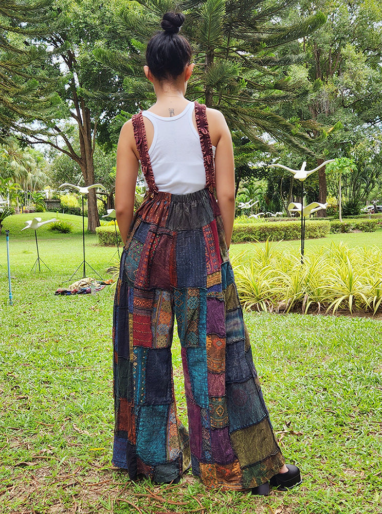 Female model wearing brown patchwork overall jumpsuit in a park, back view.