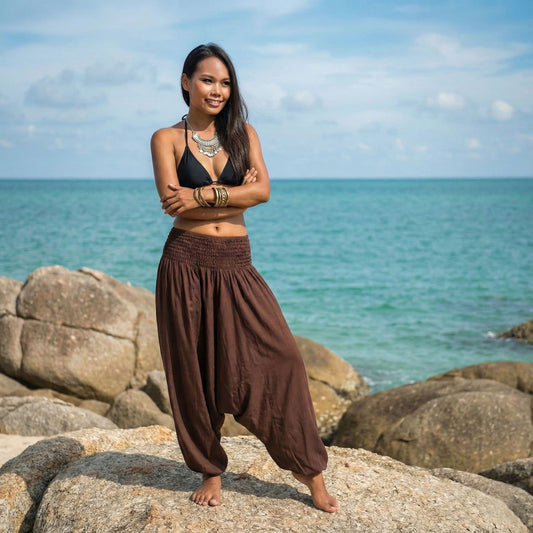 Woman standing on rocks by the ocean with a blue sky waering a brown 2-in-1 jumpsuit harem pants and black bikini top
