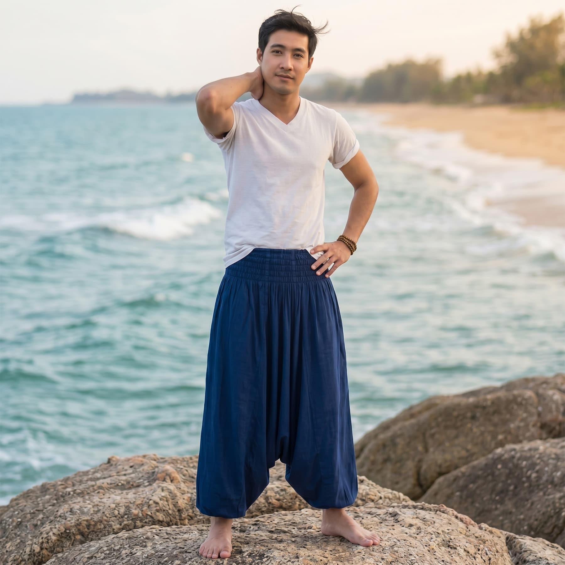Male model on rocks at a tropical Thai beach wearing deep navy blue Men's drop crotch harem pants.