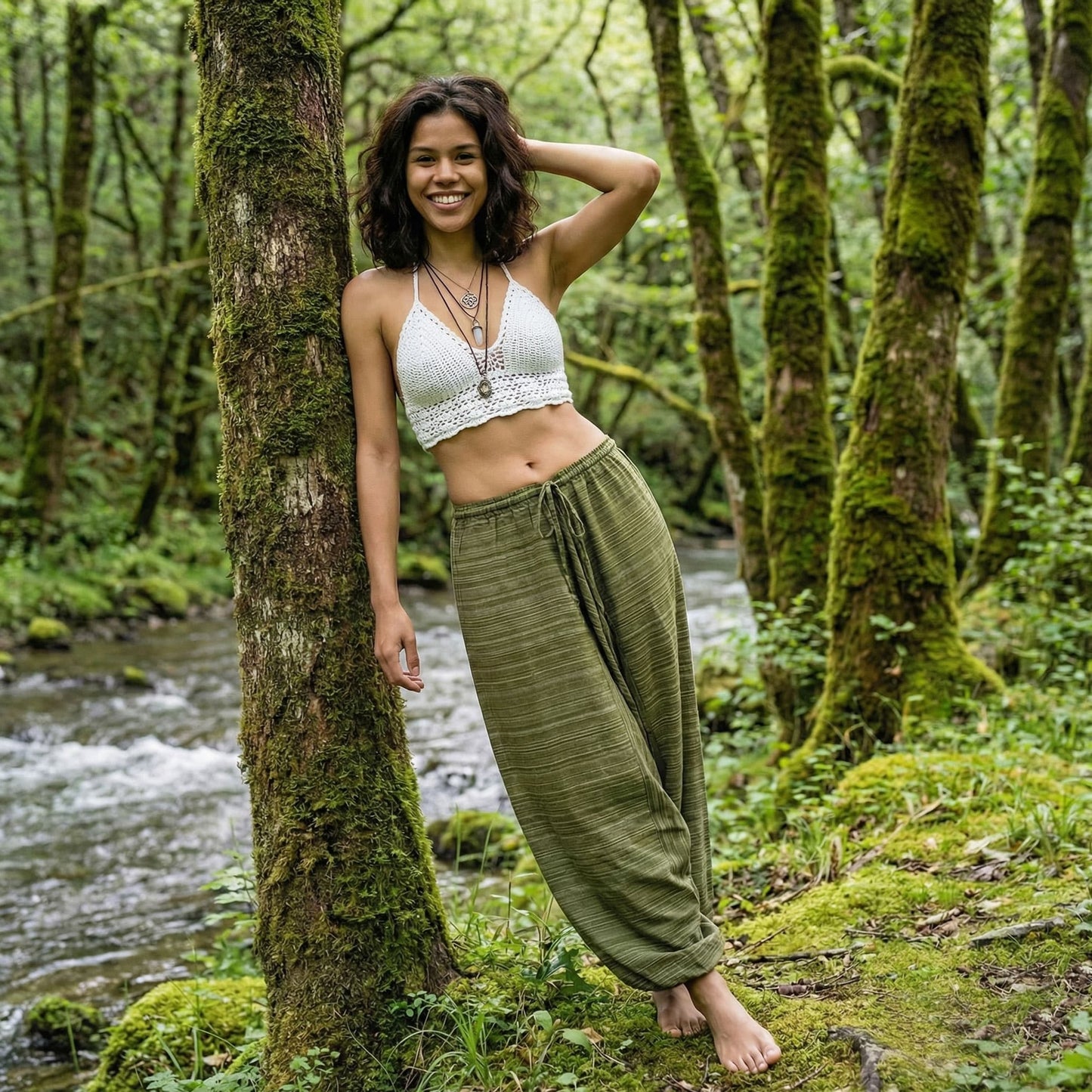 Woman in a white top and green pinstripe thai harem pants standing in a forest by a stream
