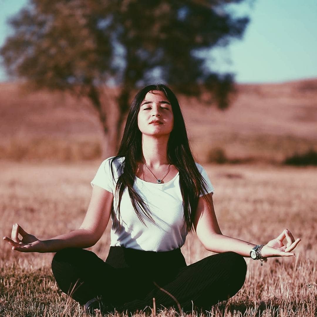 Woman wearing a black my thai harem pants meditating in a field with trees in the background