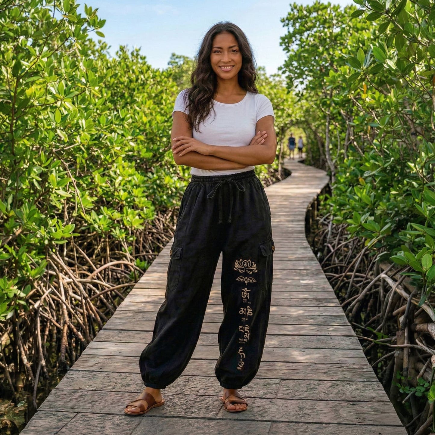 Woman posing in black boho stonewashed lotus festival harem pants on a wooden bridge, showing the functional pockets.