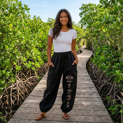 Female model wearing black boho lotus festival harem pants on a boardwalk through mangroves, front view.