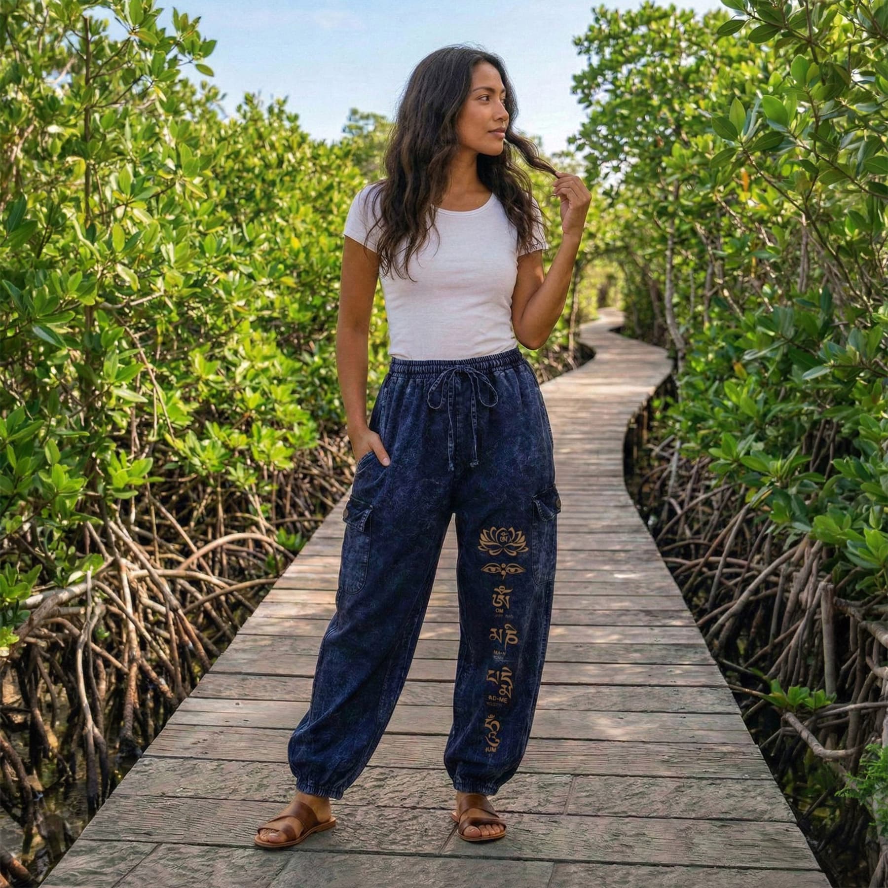 Female model wearing blue boho lotus festival harem pants on a boardwalk through mangroves, front view.