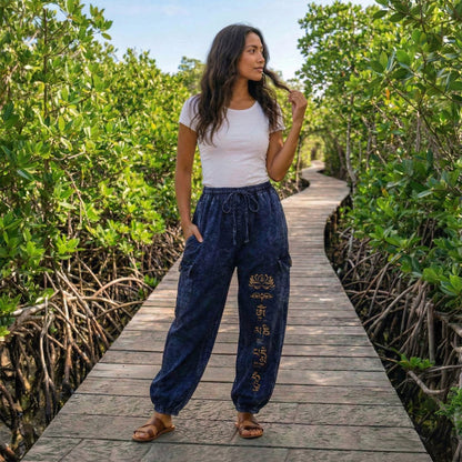 Female model wearing blue boho lotus festival harem pants on a boardwalk through mangroves, front view.