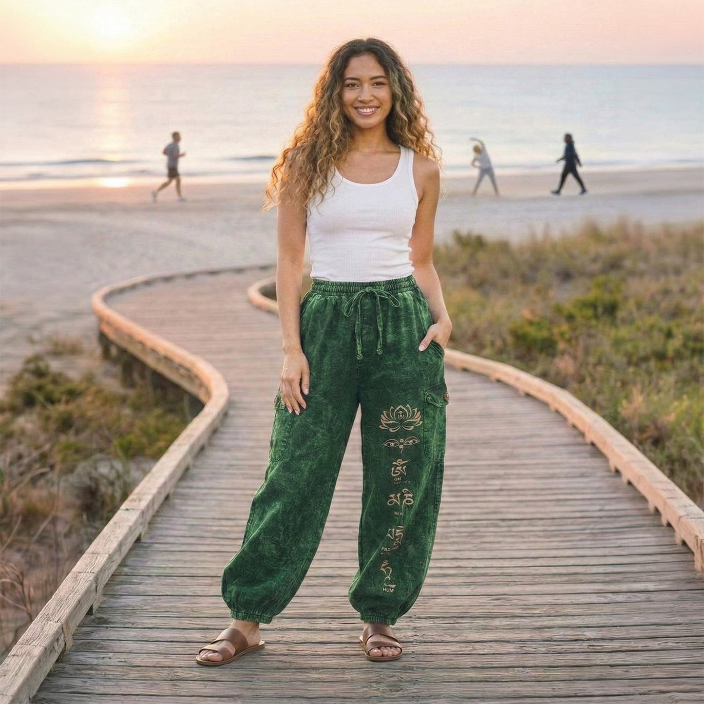 Woman posing in green boho stonewashed lotus festival harem pants on a beach walkway, showing the four-pocket design.