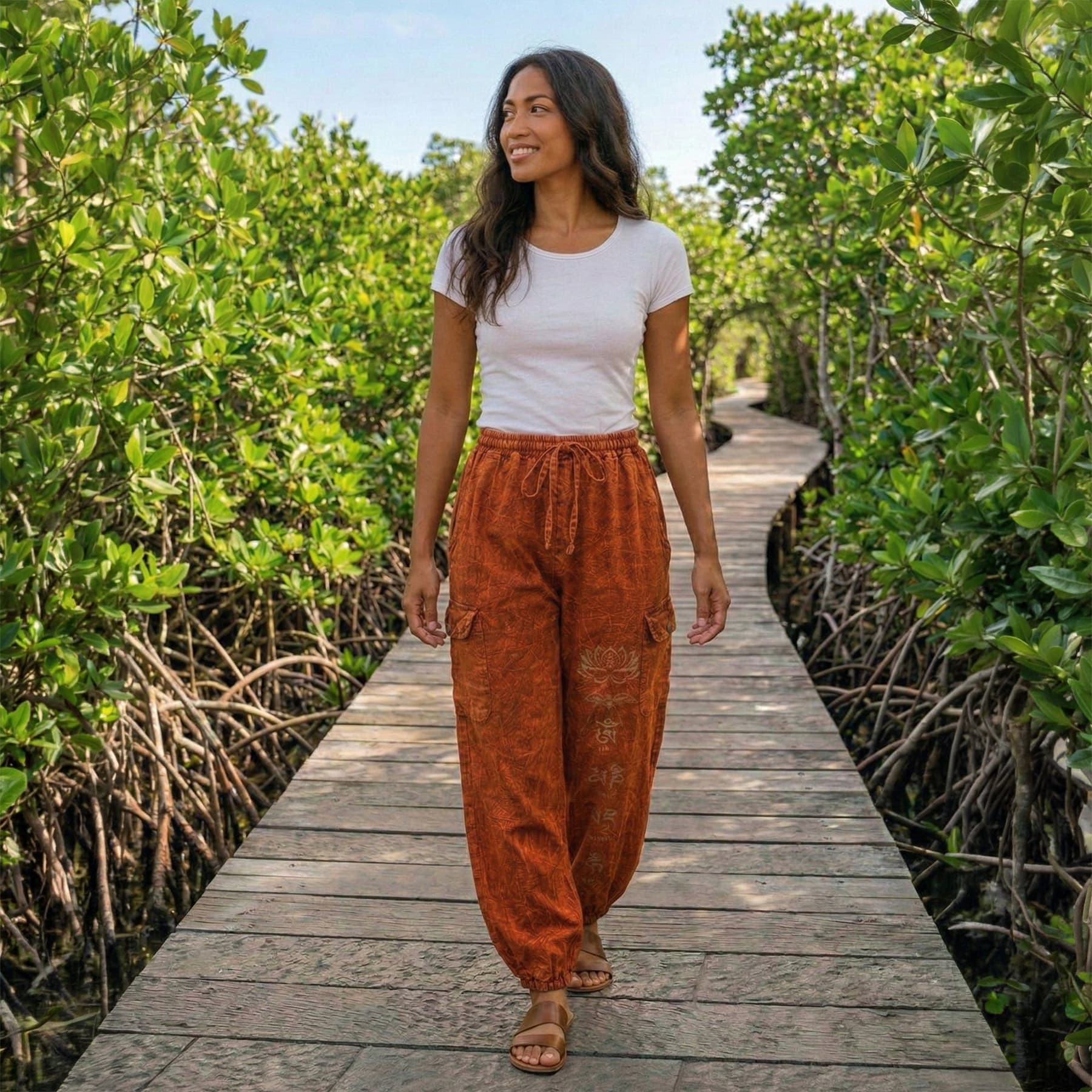 Woman posing in orange boho stonewashed lotus festival harem pants on a wooden bridge, showing the four-pocket storage.