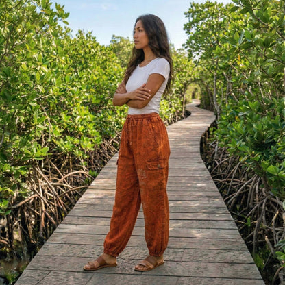 Side view of orange boho lotus festival harem pants on a boardwalk highlighting the stitched cargo pocket.