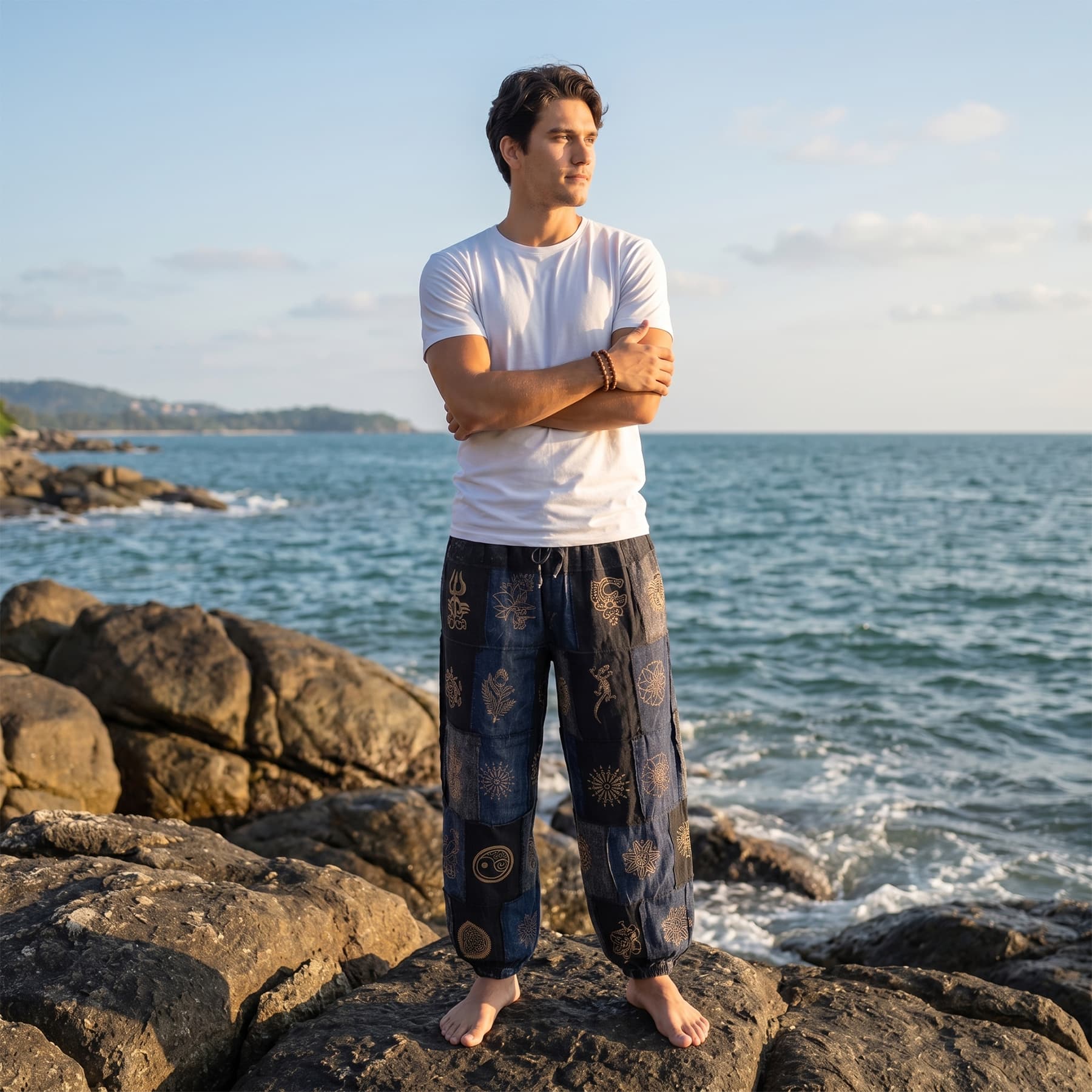 Male model enjoying the breeze on beach rocks in black stonewashed organic cotton tribal harem pants.